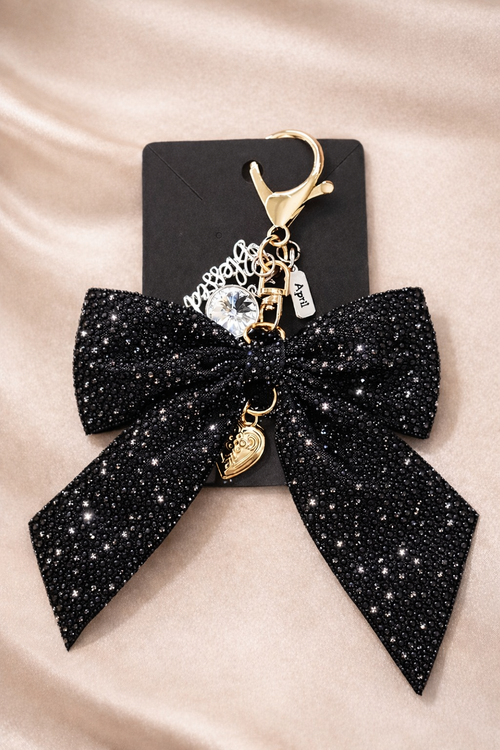 Black glittery bow keychain with gold charms on a beige satin background